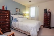 A neatly decorated bedroom with a bed, matching dressers, and a window letting in light.