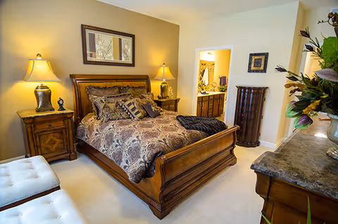 Cozy bedroom featuring a wooden sleigh bed with patterned bedding, nightstands with lamps, and an open doorway to a bathroom.
