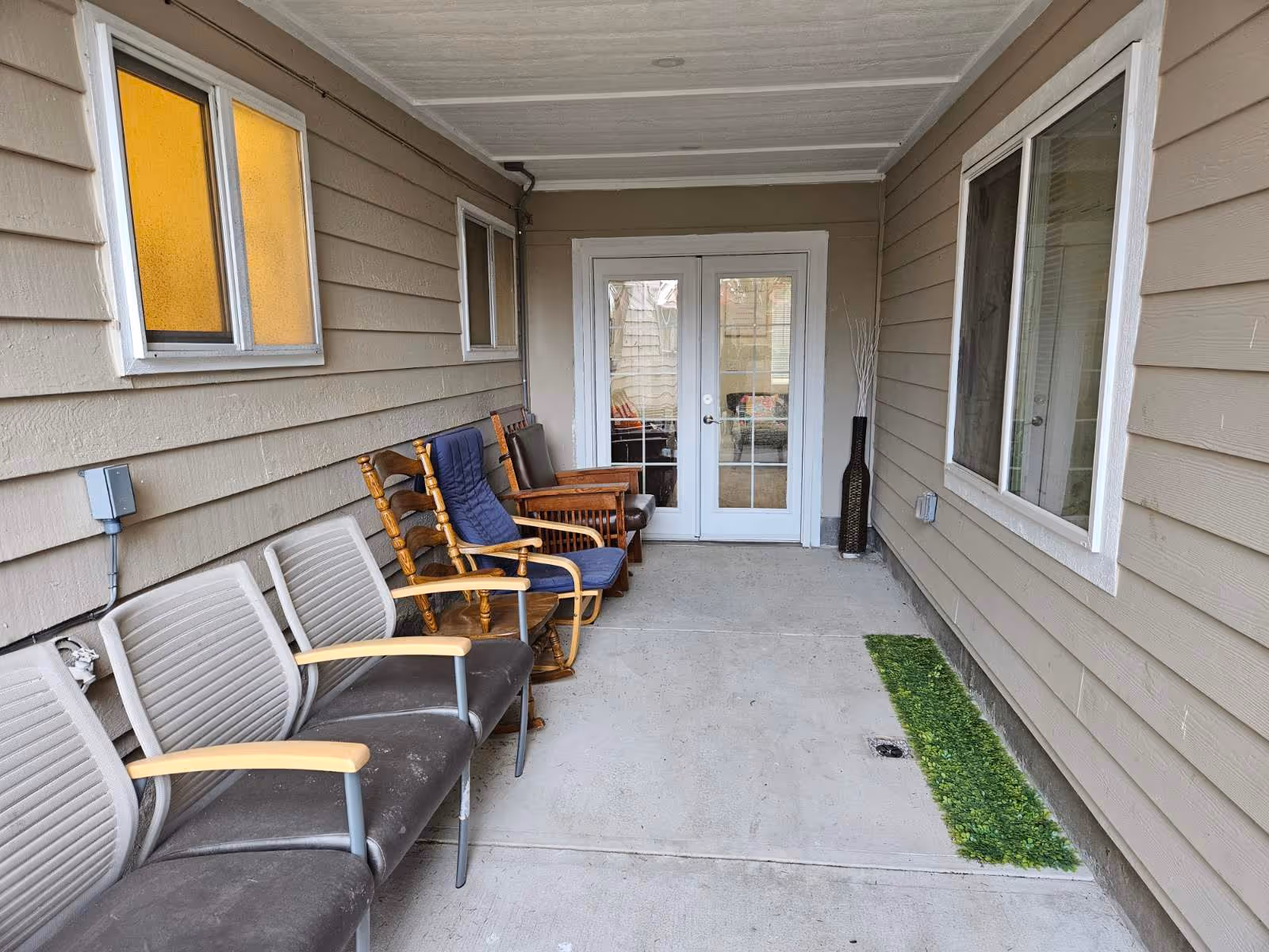 Covered exterior porch with a row of chairs and rocking chairs facing a set of glass-paneled double doors.