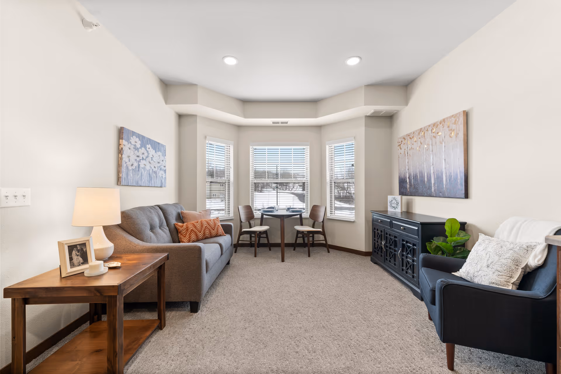 Bright furnished living room with a sofa, armchair, side table and a bay-window seating area.