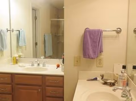 Bright bathroom with double sinks, wooden cabinets, mirrors, and towels hanging on racks.