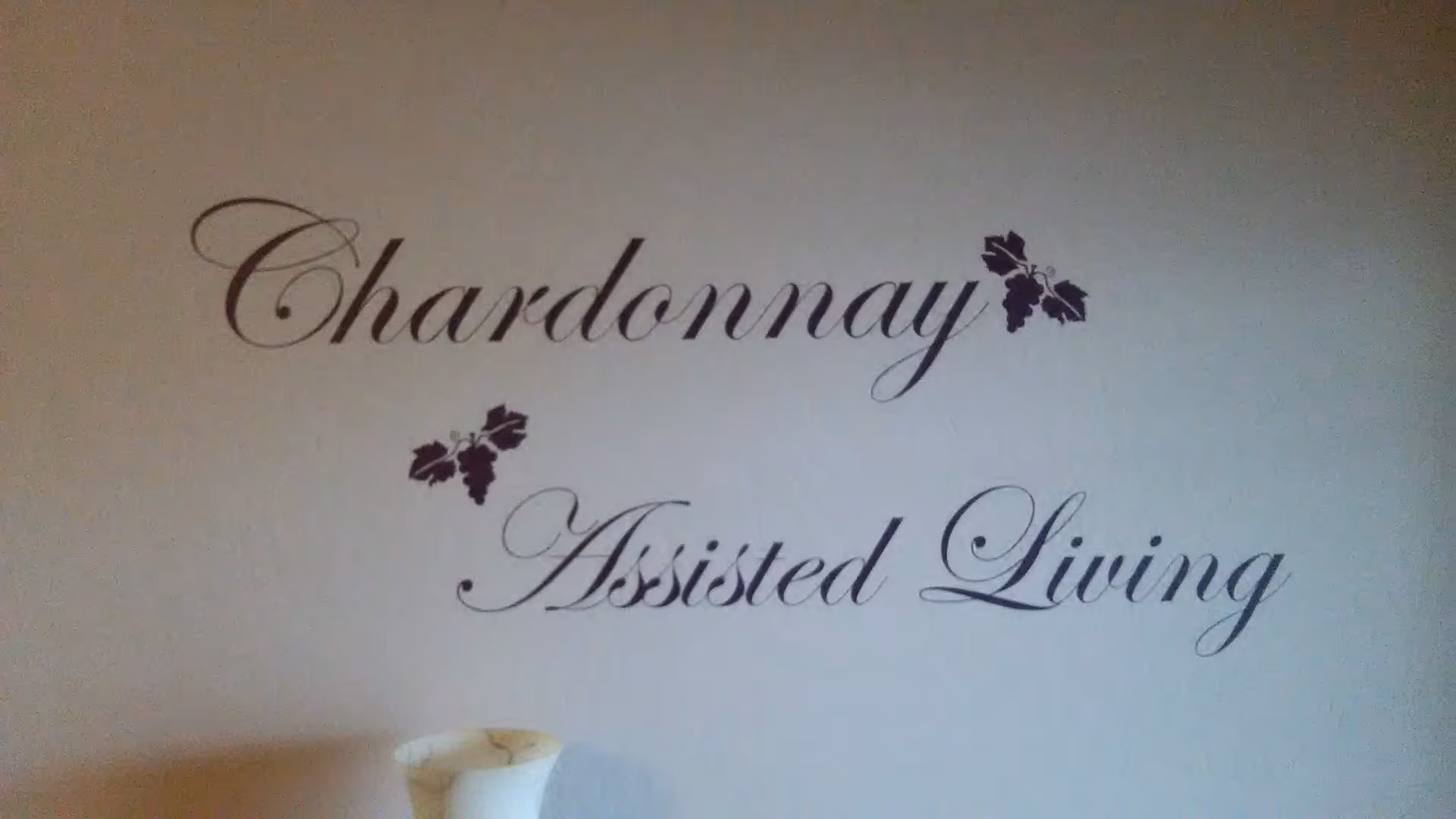 A decorative wall sign reading "Chardonnay Assisted Living" in script with small grape motifs.