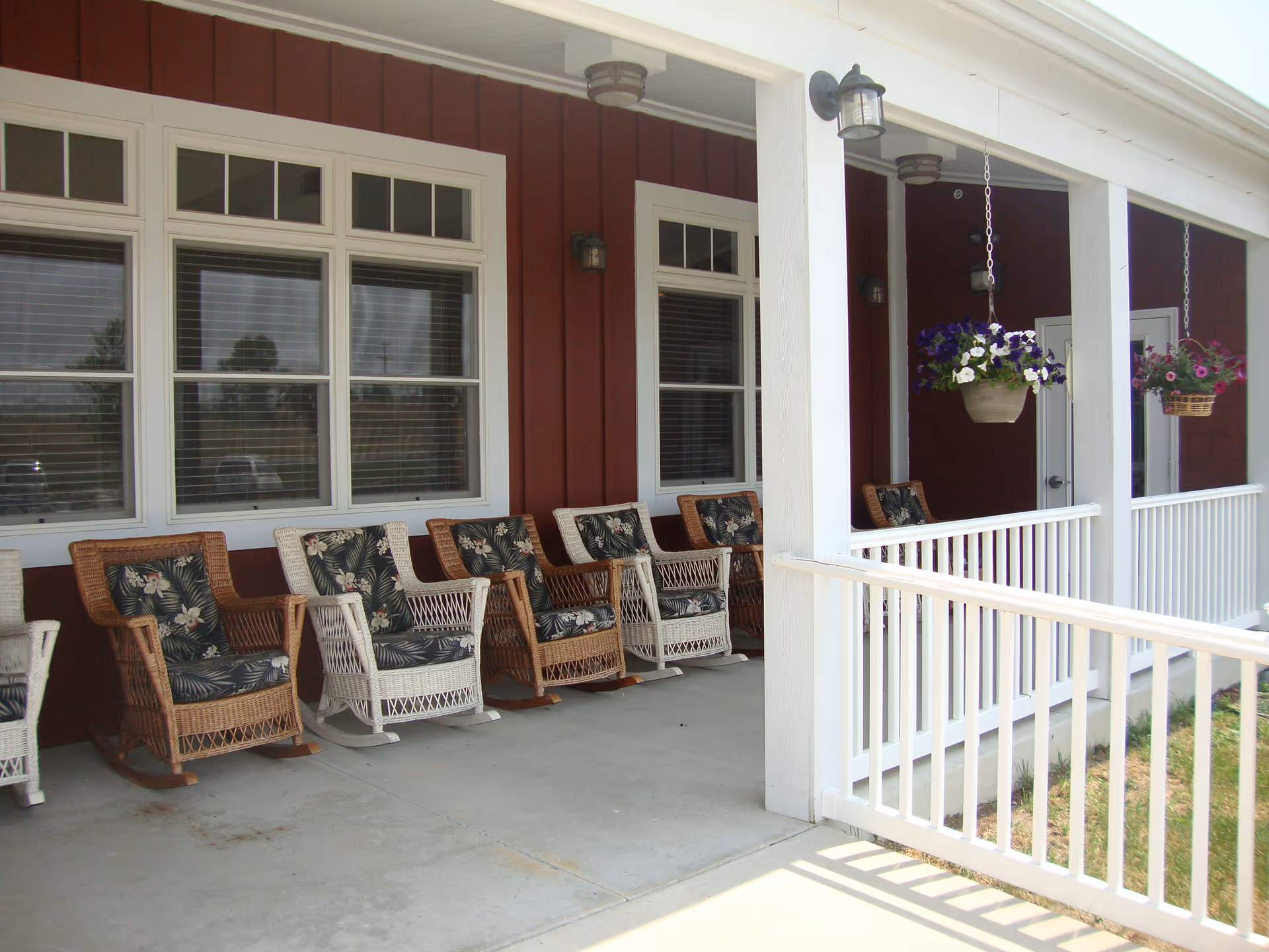 Covered front porch with a row of wicker rocking chairs and hanging flower baskets on a red building.