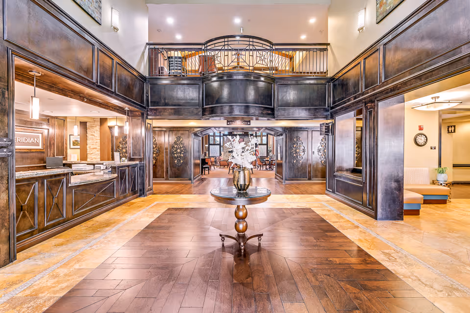 Bright, elegant two-story lobby with a central round table, dark wood paneling, a reception desk to the left and seating areas beyond.