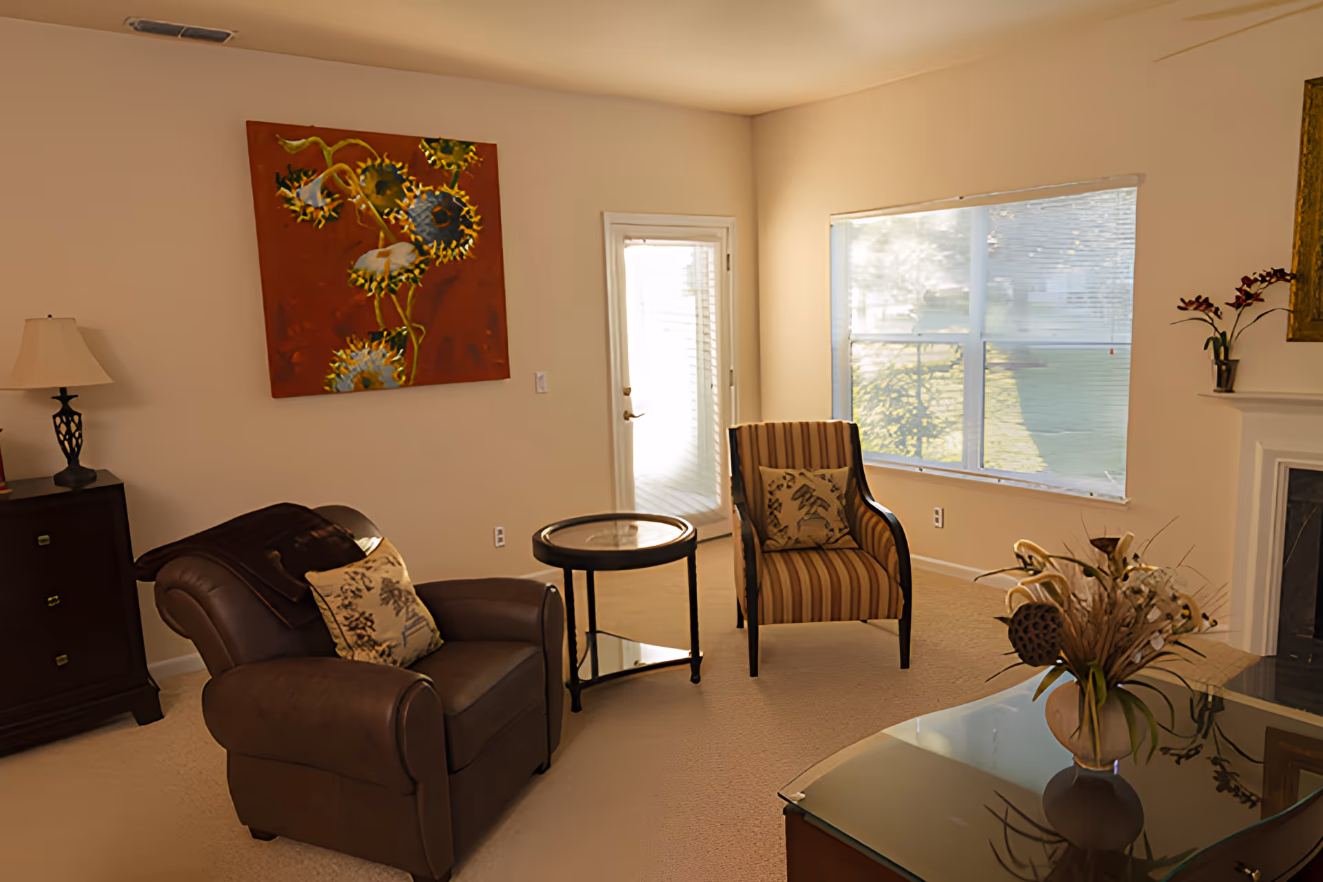 Sunlit living room with a leather armchair, striped accent chair, coffee tables, wall art, and a large window.