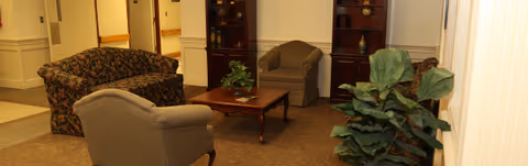 Cozy lounge in a senior facility with couches, chairs, a coffee table, and plants.