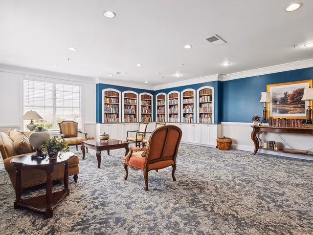 Bright communal lounge with upholstered chairs, coffee tables, and built-in bookshelves along a blue accent wall.