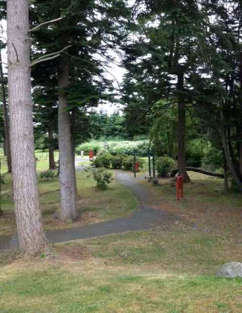 Path winding through a grassy, tree-filled outdoor area with red posts.