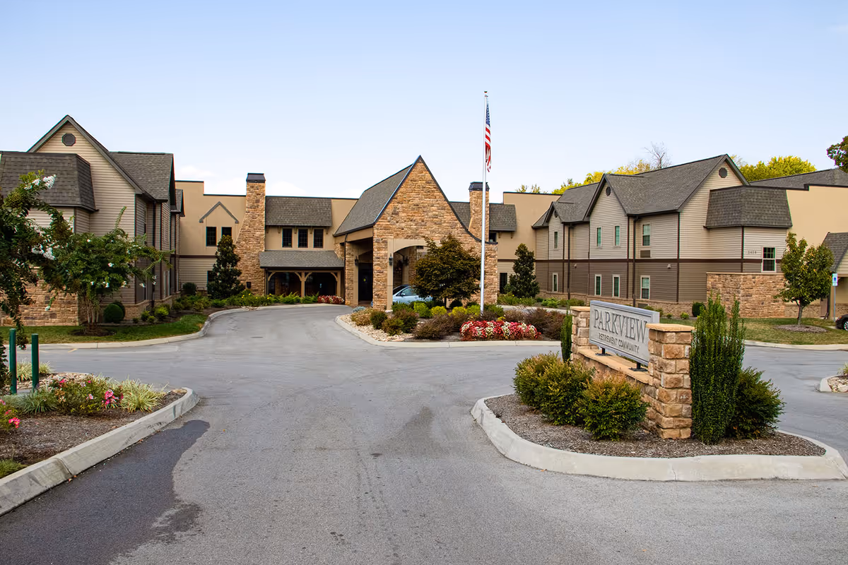 Front view of Parkview Senior Living building with a circular driveway, landscaped island, American flag, and a stone entrance sign.