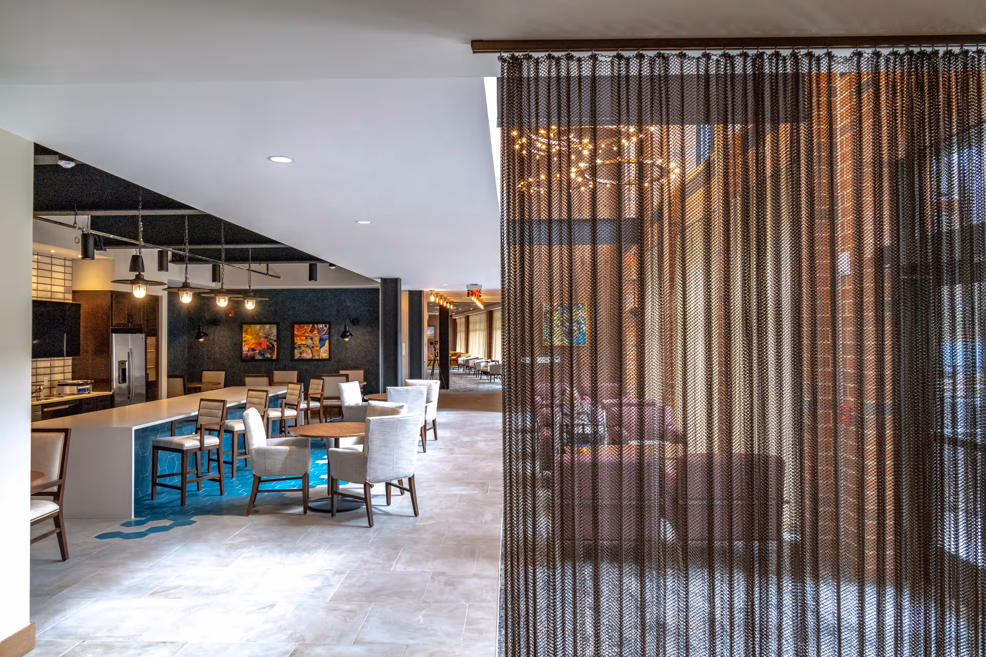 Open interior common area with a long bar and dining tables on the left and a sheer curtain partition revealing a lounge on the right.
