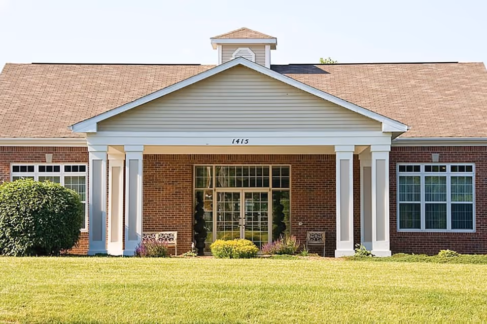 Front entrance of a single-story brick building with white columns, a gabled portico and glass double doors.