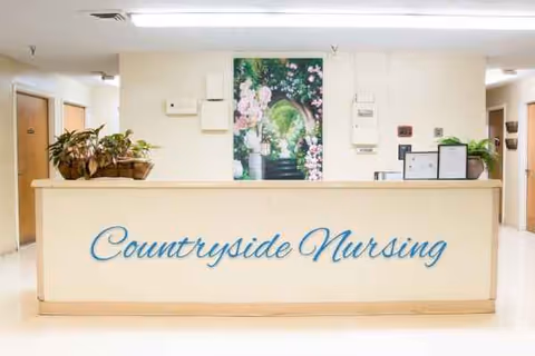Reception desk with a Countryside Nursing sign, potted plants, and a floral poster in a lobby.