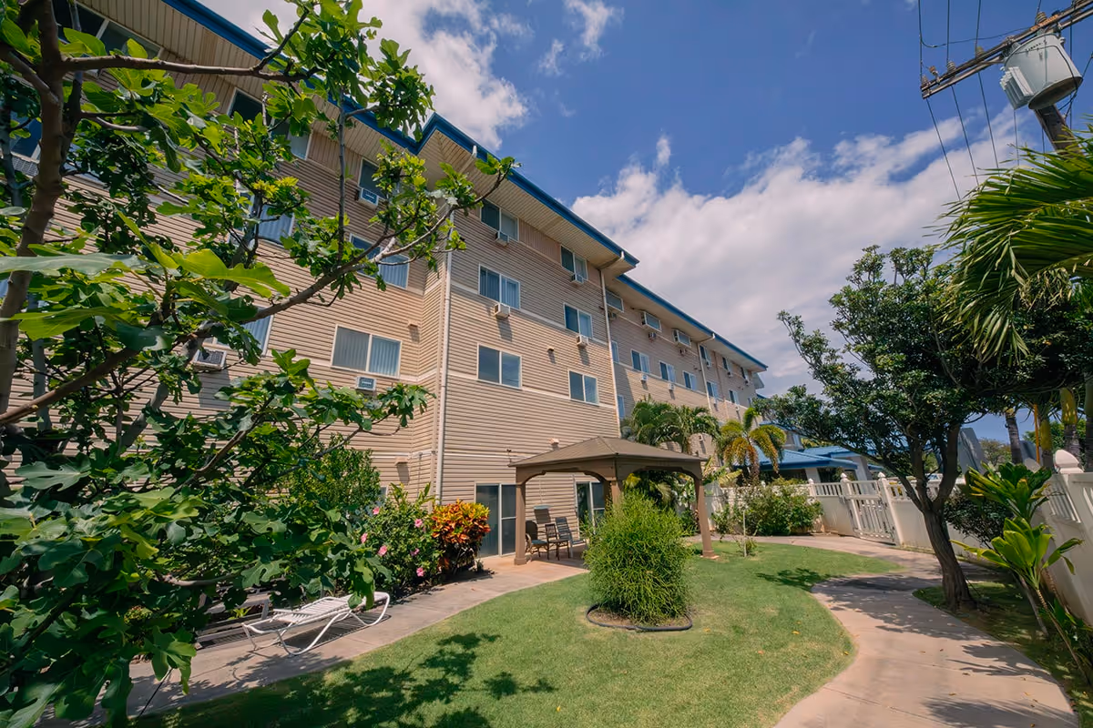 Landscaped courtyard with lawn, gazebo and seating in front of a multi-story beige building under a blue sky.