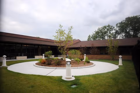 Circular courtyard with a landscaped center, white lamp posts and surrounding single-story building under a cloudy sky.