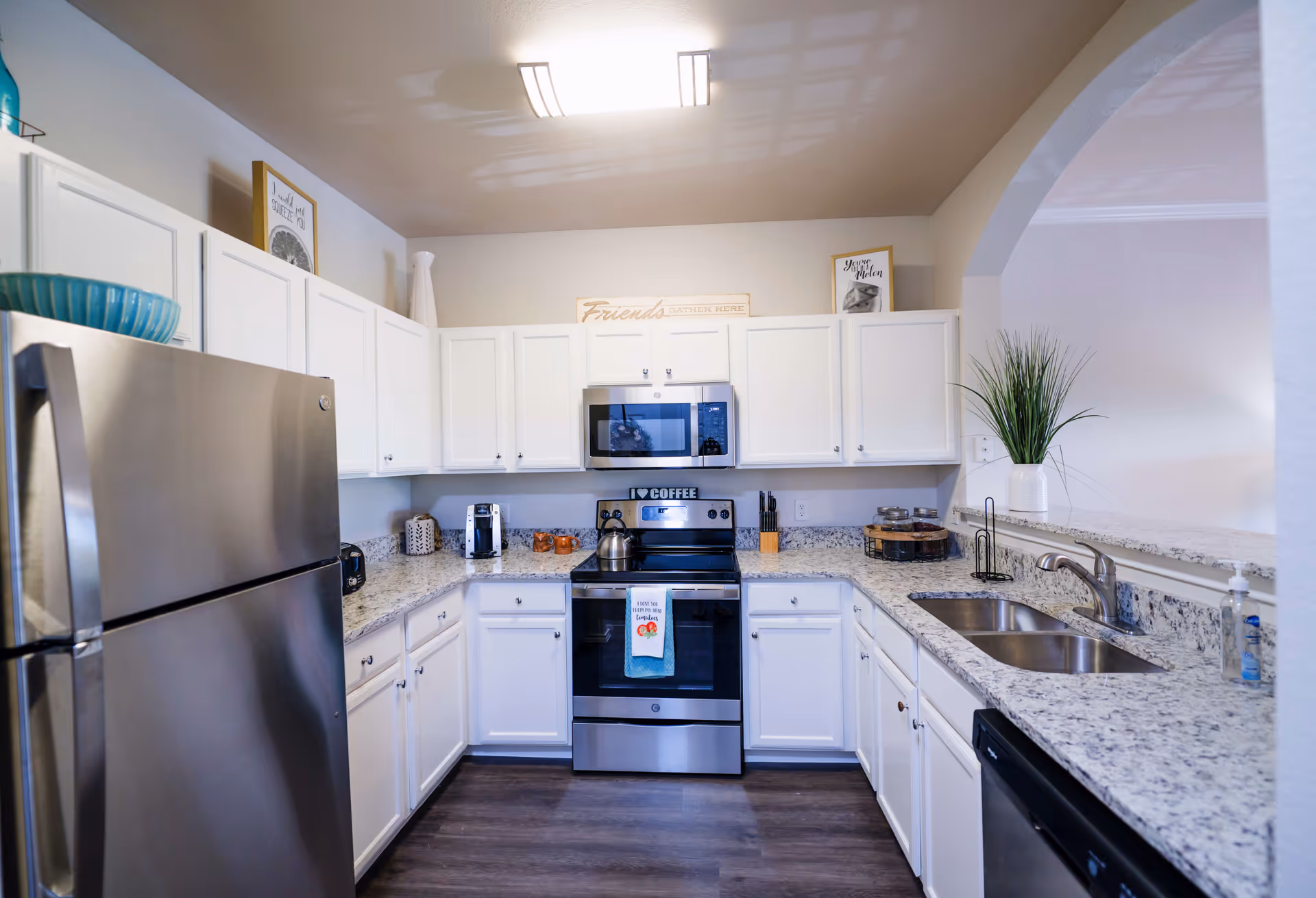 Bright kitchen with white cabinets, stainless steel refrigerator and stove, granite countertops and a double sink.