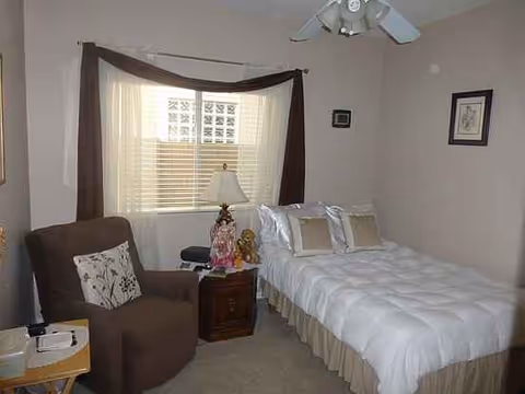 A cozy bedroom with a bed, armchair, nightstand, lamp, and window with curtains.