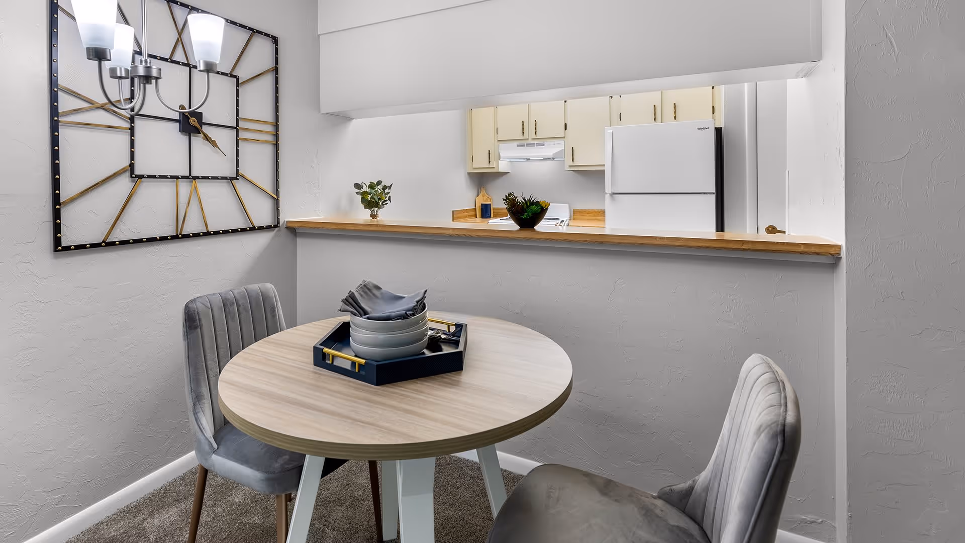 Small dining area with a round table, two upholstered chairs, and a pass-through counter to a kitchen.