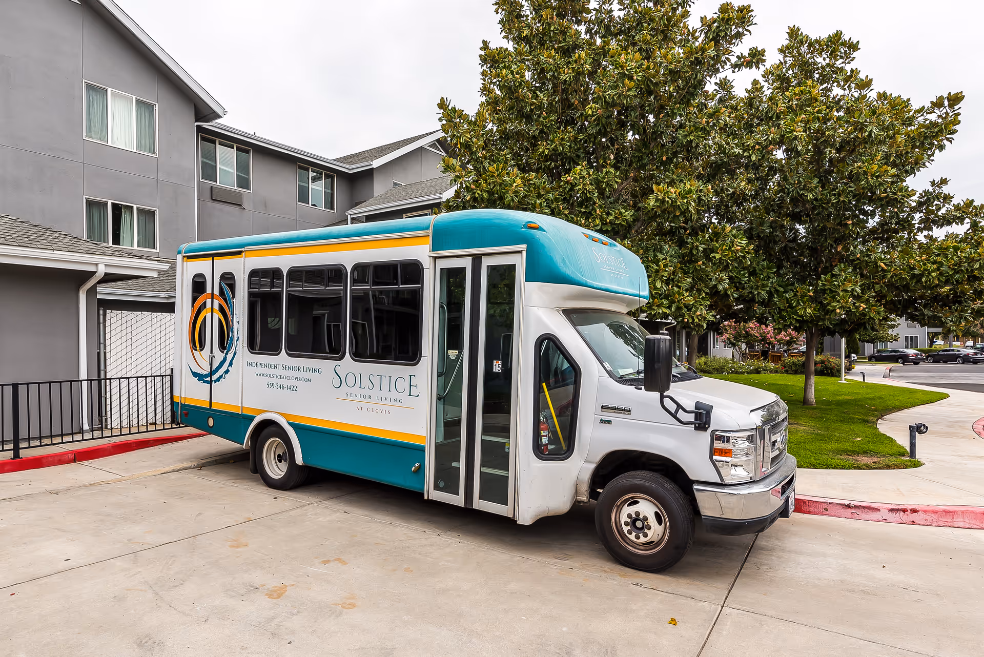 A teal-and-white Solstice Senior Living shuttle bus parked outside the senior living building under trees.