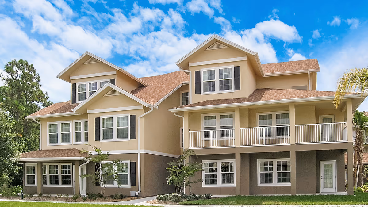 Multi-story beige residential building with multiple windows, balconies and gabled roofs under a blue sky.