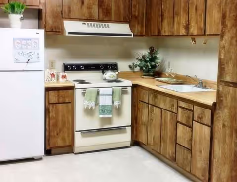 Cozy residential kitchen with wooden cabinets, stove, fridge, and sink in a senior living setting.