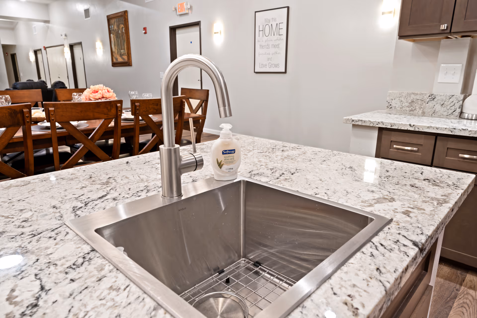Kitchen island with a stainless steel sink and faucet on a granite countertop, with a dining table visible in the background.