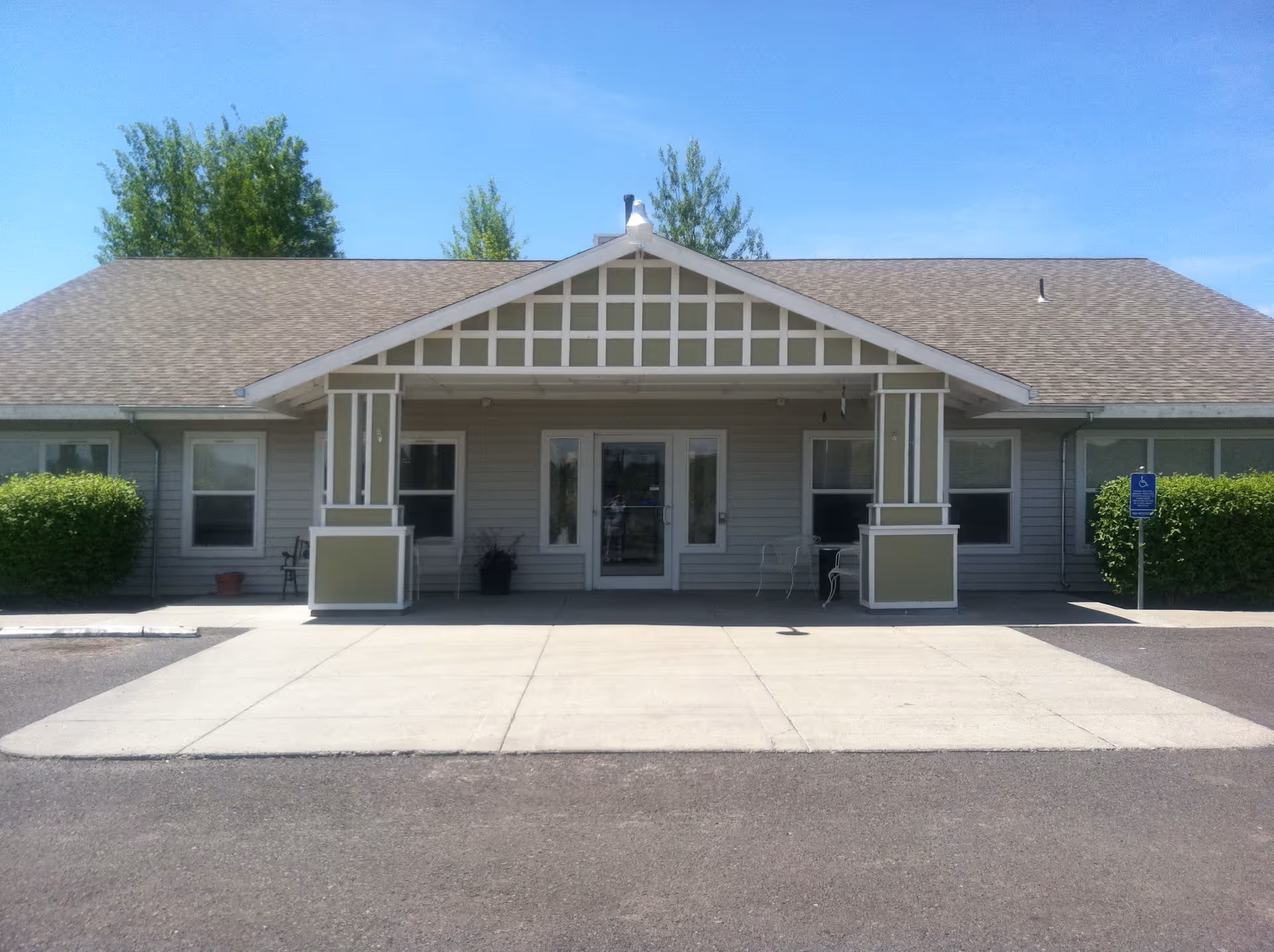 Single-story building front with a covered entrance featuring two square columns, double glass doors, and a paved driveway.
