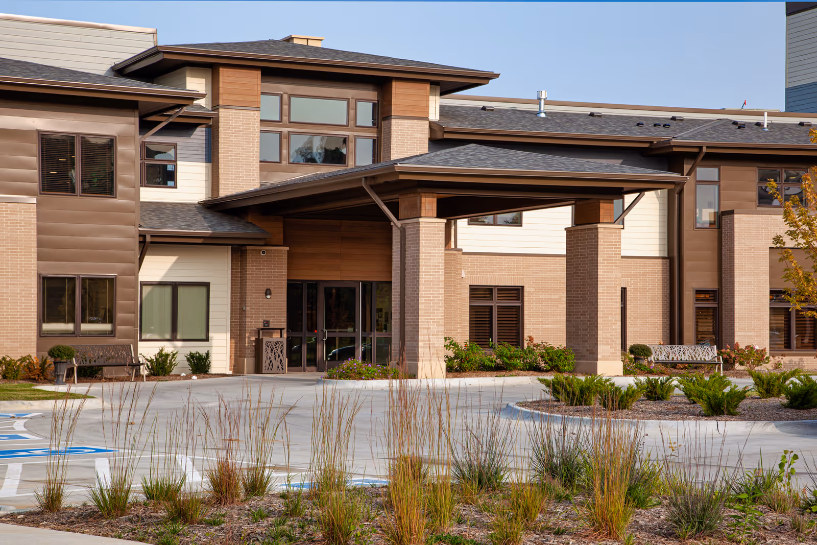 Front entrance of a senior living facility with a covered portico, brick facade, windows, and landscaped driveway.