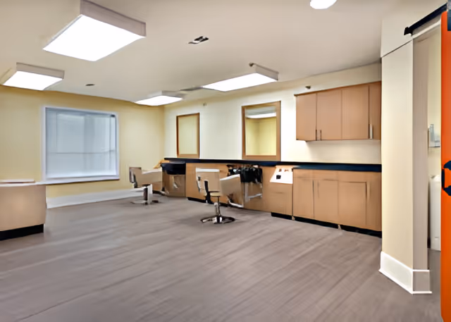 Bright salon-style interior with styling chairs, mirrors, and cabinetry in a senior living facility.