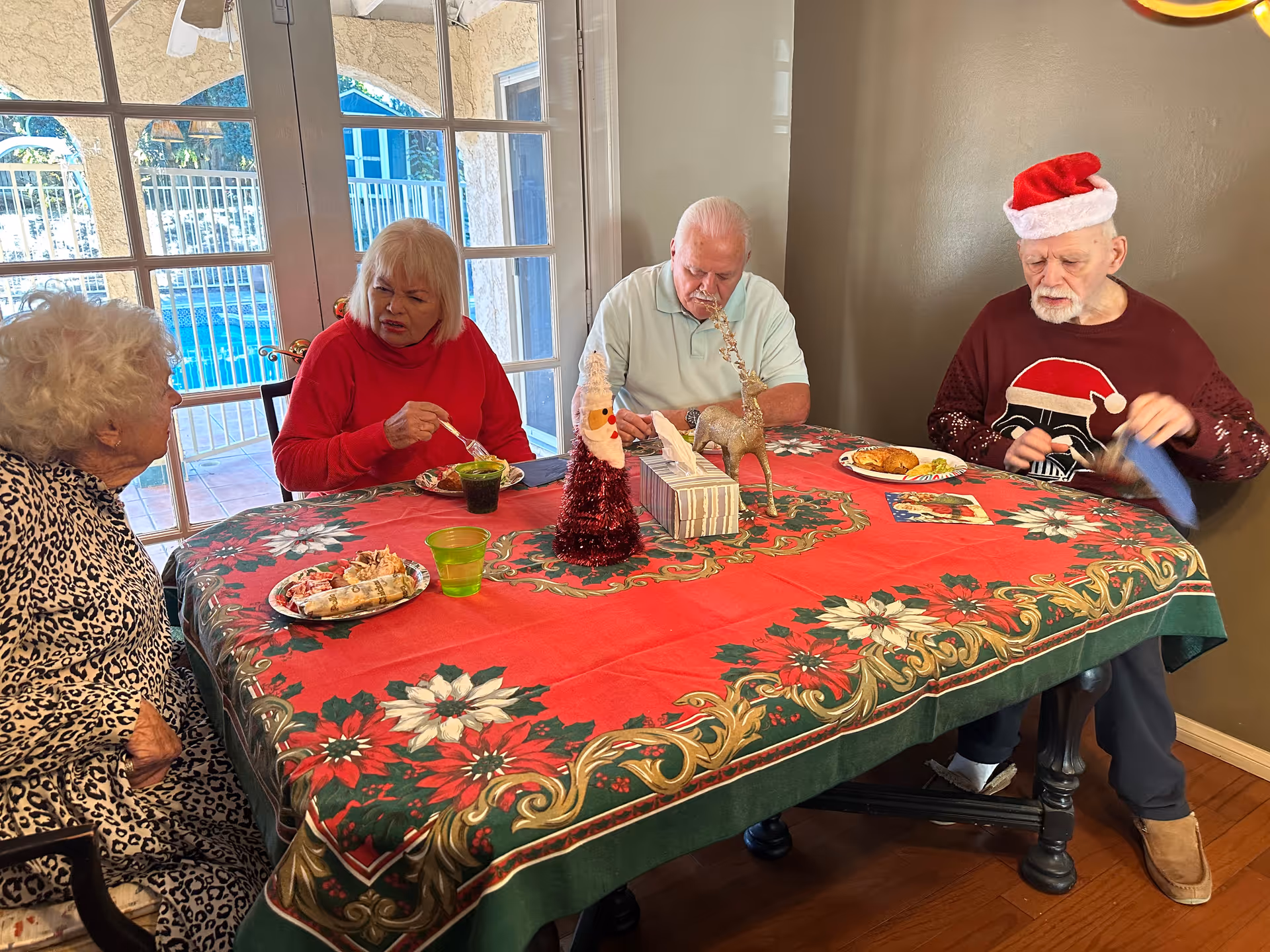 Four elderly people seated around a festively decorated dining table, eating and conversing.