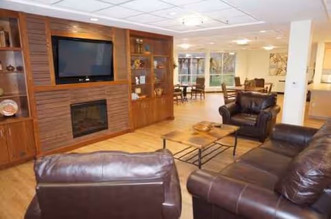 Cozy senior living lounge with leather sofas, coffee tables, and a wall mounted TV.