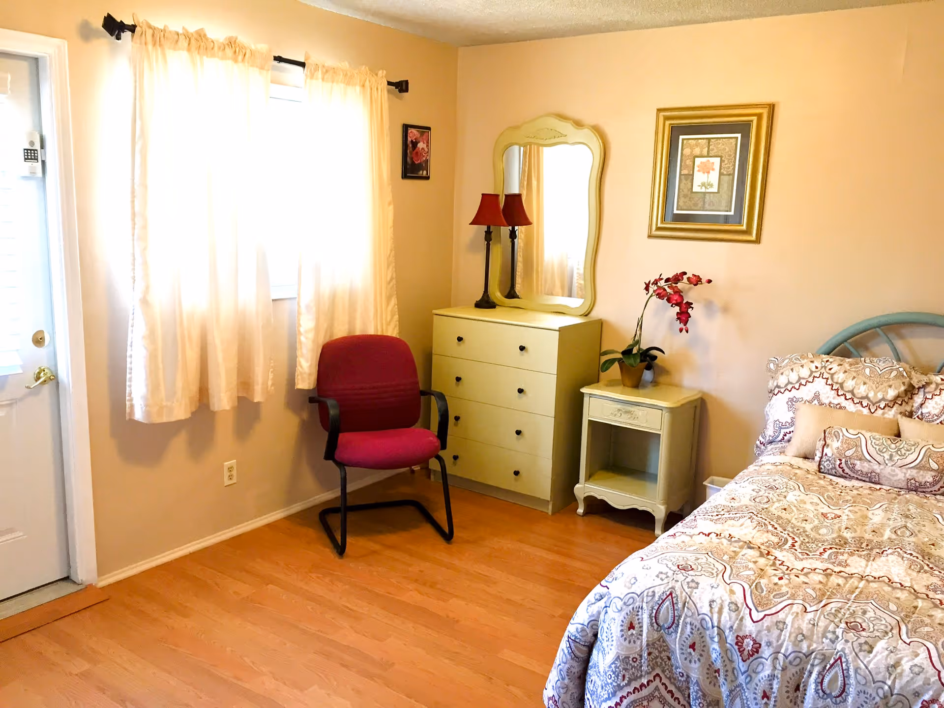 A cozy bedroom with a bed, dresser, mirror, and a chair beside a window.