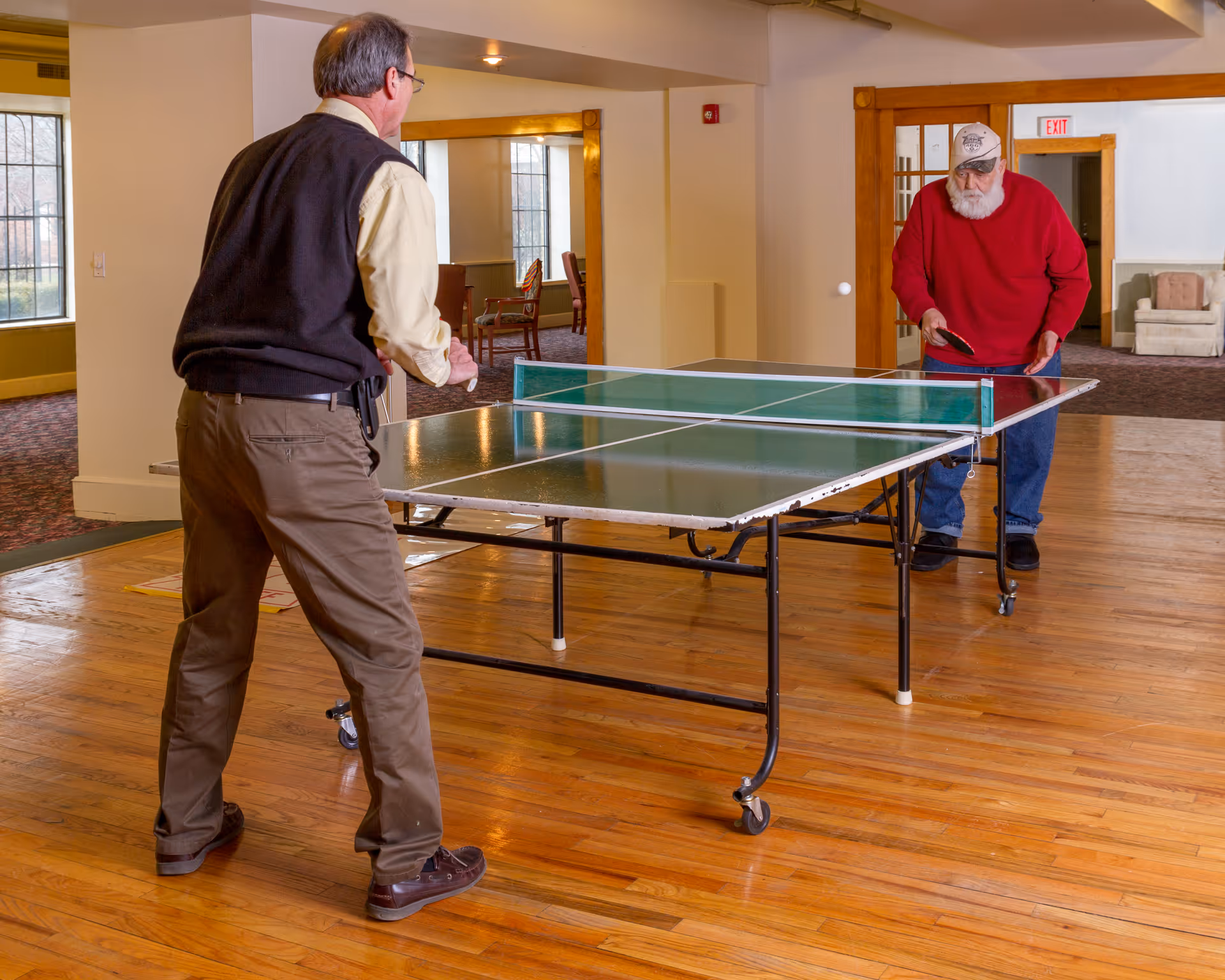 Two men playing table tennis in a communal indoor recreation room.