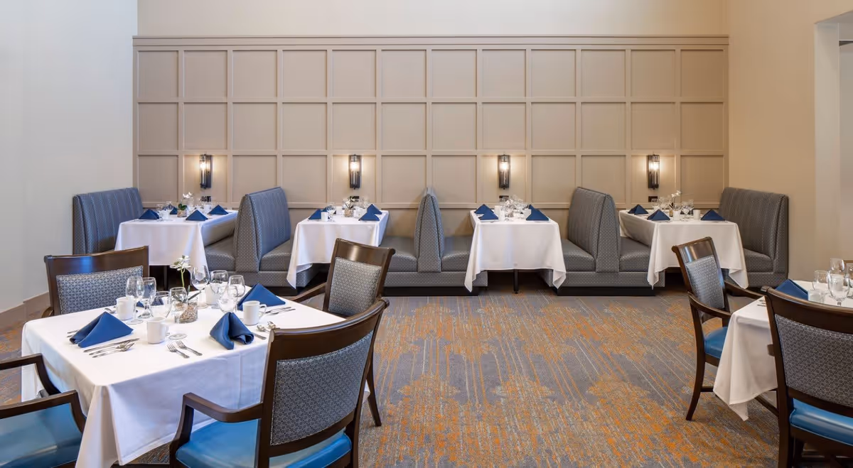 Well-lit dining room with upholstered booths and tables set with white linens, blue napkins, glassware, and place settings.
