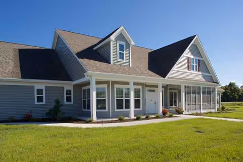 A cottage-style senior living facility front with a covered porch and green lawn.
