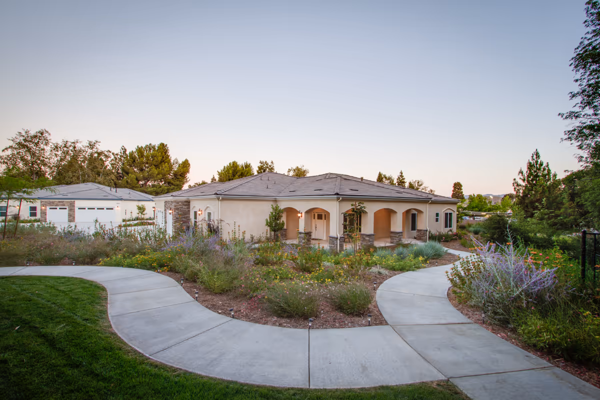 Single-story Mediterranean-style building with an arched porch surrounded by landscaped gardens and curved concrete walkways.