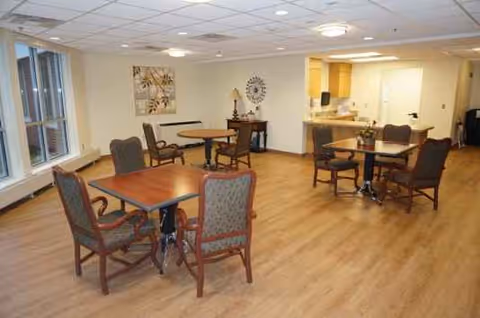Interior common area with wooden floors, round dining tables and chairs in a senior facility.