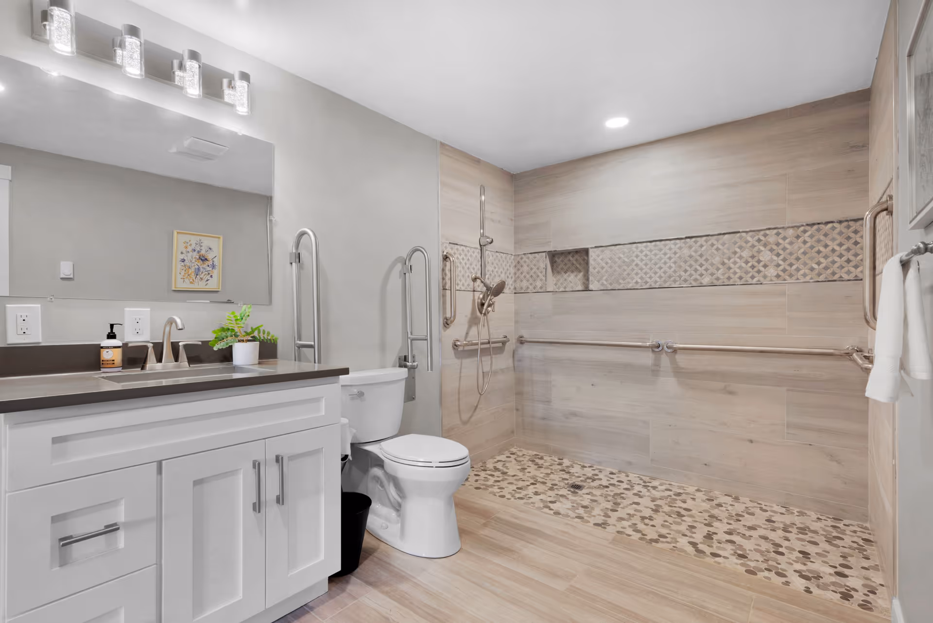 Accessible modern bathroom with a vanity and sink, toilet, and a walk-in shower with grab bars and pebble-tiled floor.