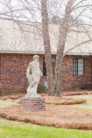 Stone statue on brick pedestal stands before Pembroke Center building with trees.