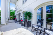 Outdoor patio area at The Trace featuring a row of black rocking chairs and potted plants along the building's exterior wall with large white columns and windows reflecting greenery.