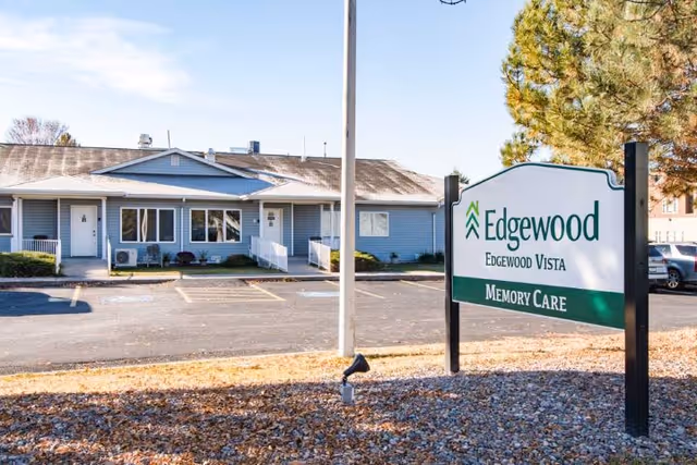 A freestanding sign reading "Edgewood Edgewood Vista Memory Care" stands in front of a single-story light-blue memory care building and parking lot.