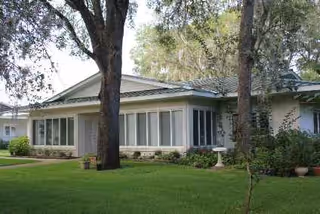 Single-story senior living facility with large windows, a manicured lawn, and trees.