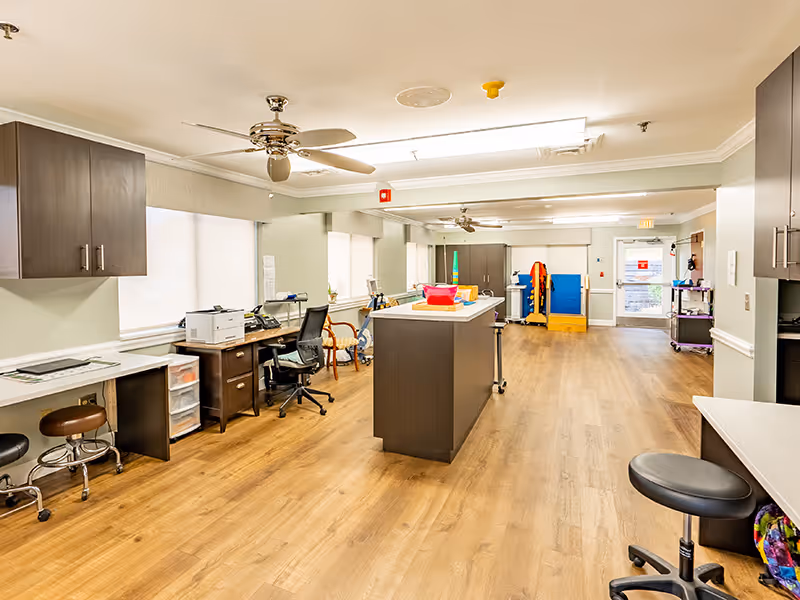 Interior view of Brushy Creek Post Acute showing a spacious room with wooden flooring, desks, chairs, and large windows.