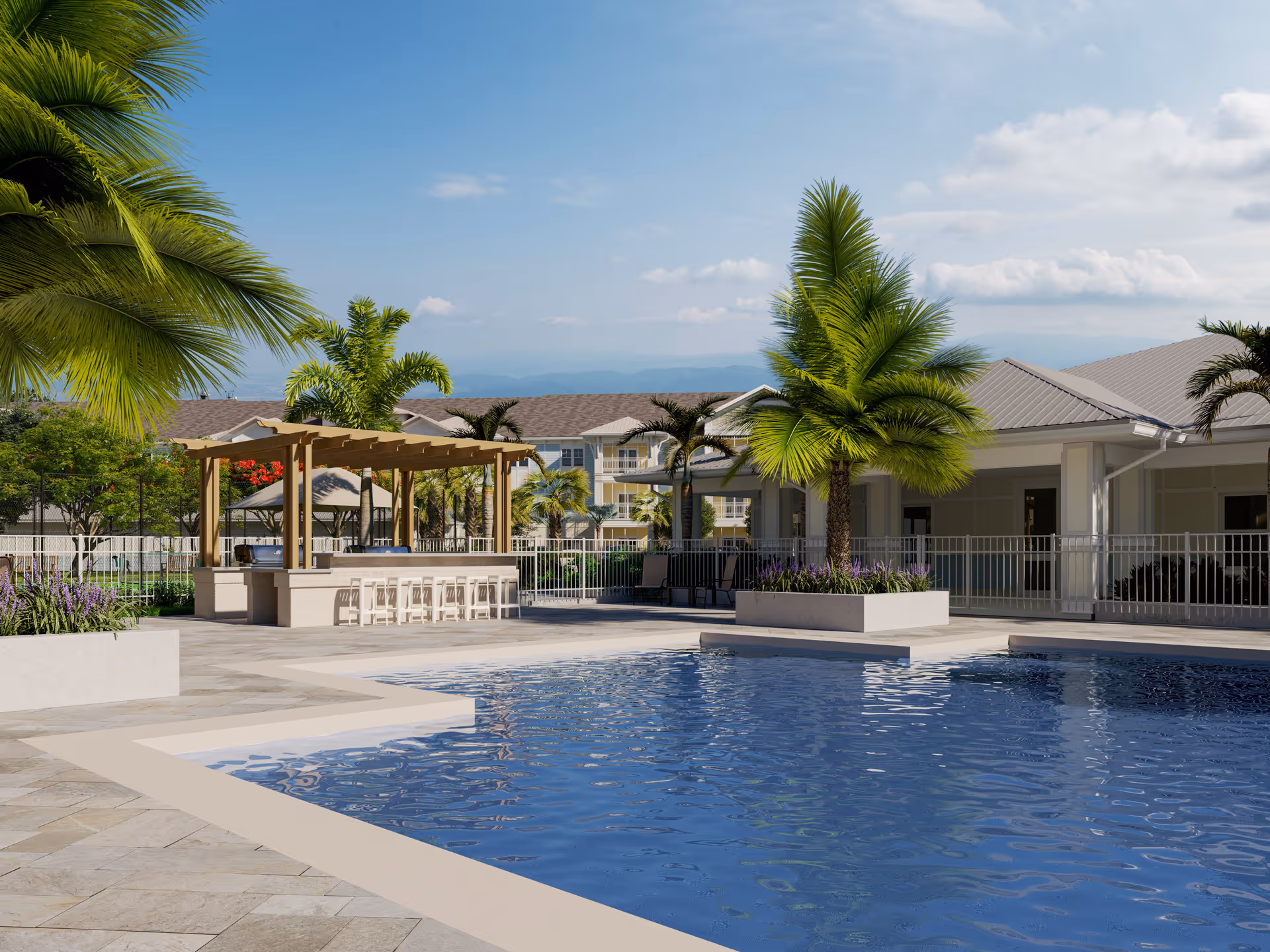 Outdoor pool area with clear blue water, surrounded by tiled flooring and palm trees. There is a wooden pergola with bar stools underneath and a building with a covered patio in the background under a partly cloudy sky.