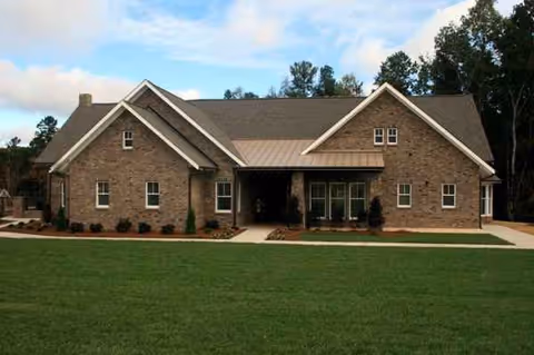 Brick senior living facility exterior with a front entrance, manicured lawn, and trees.