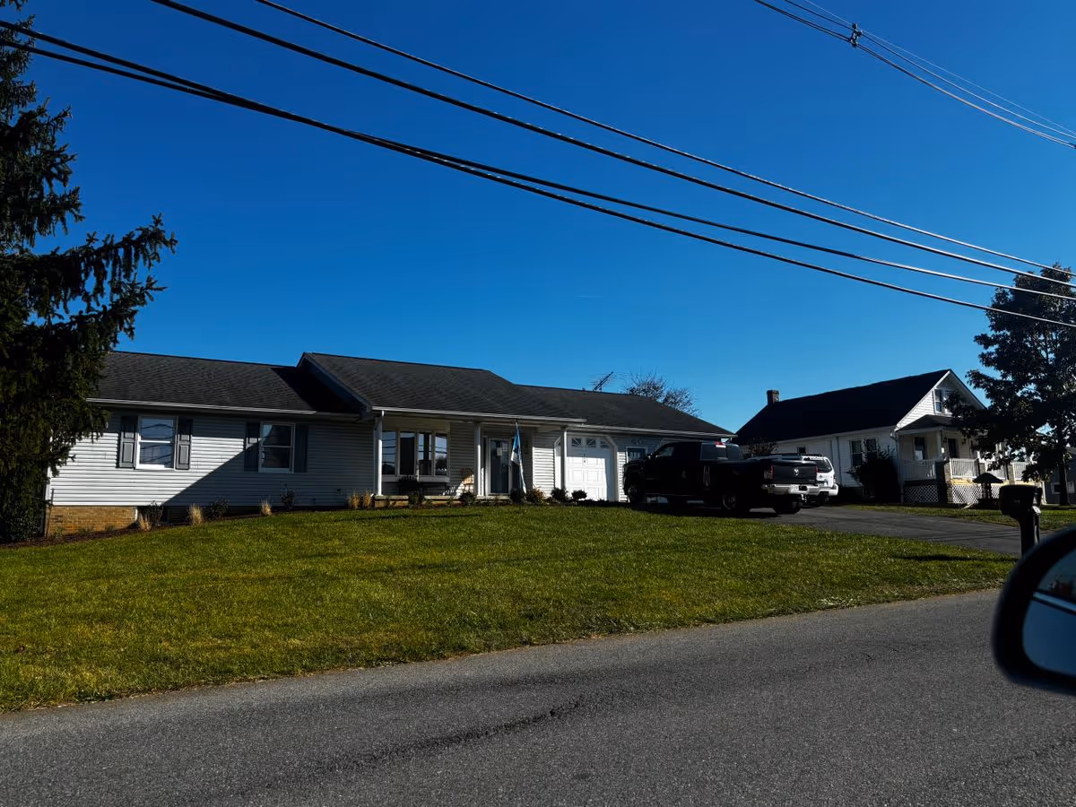 Single-story ranch-style house with a front lawn and parked trucks under a clear blue sky.