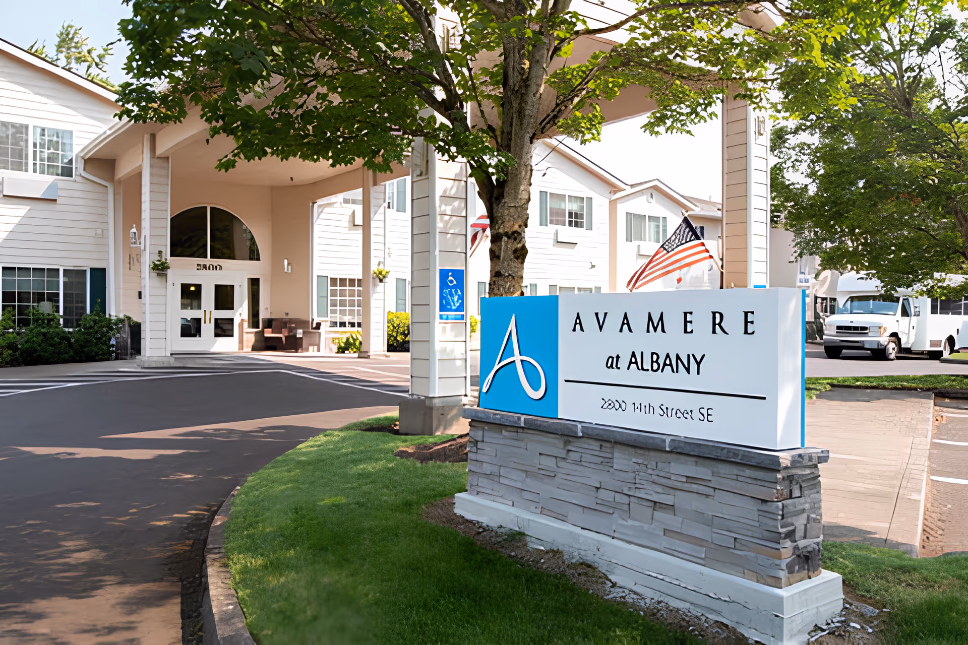Front entrance of Avamere at Albany senior living facility with a prominent sign, driveway, and building façade.