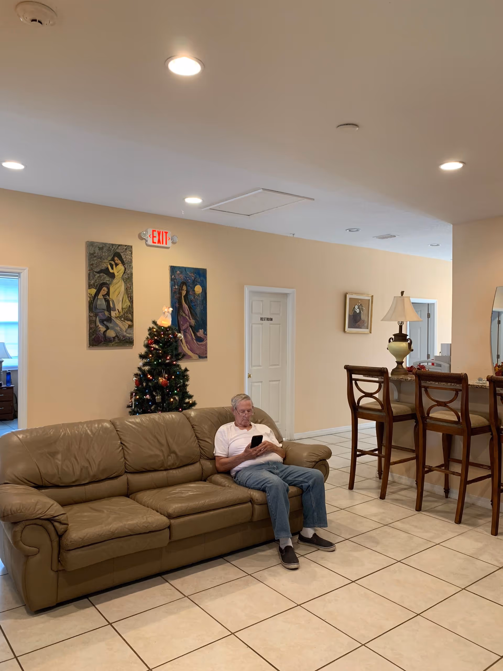 Older man sits on a tan sofa in a lobby-style living room with a Christmas tree.