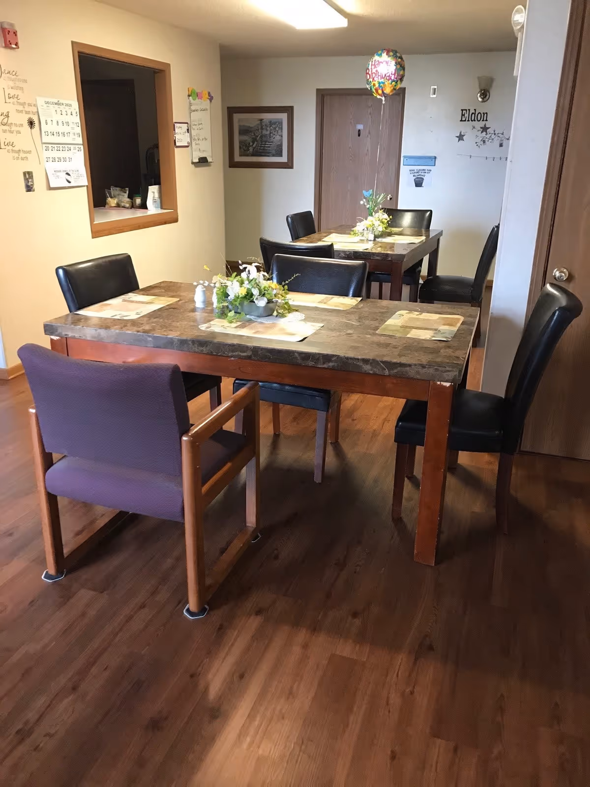 A dining area with two tables, placemats and floral centerpieces surrounded by chairs on wood floors.