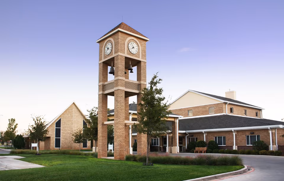 Brick building features a tall clock tower, surrounding lawn, and trees at the facility entrance.
