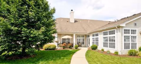 Single-story senior living facility with curved walkway, green lawn, shrubs, and large windows.